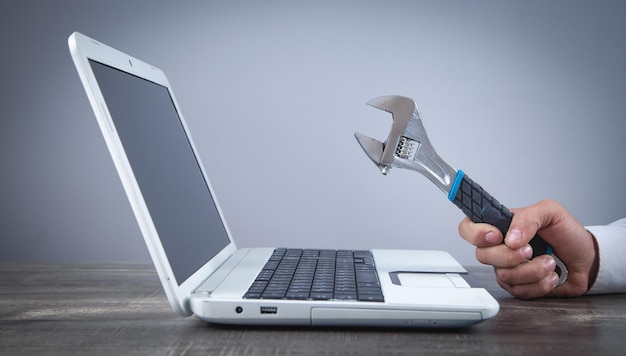 Mano masculina que muestra una llave ajustable sobre el teclado de la computadora Soporte de servicio de TI