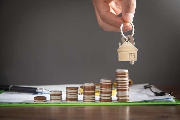 Mano masculina que muestra las llaves de la casa sobre la pila de monedas