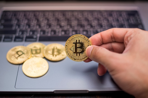 mano masculina que sostiene bitcoin en un fondo de la computadora portátil.