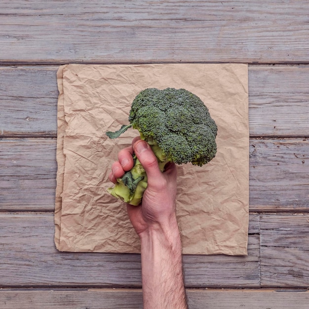 Una mano masculina que sostiene un brócoli verde fresco contra un fondo rústico