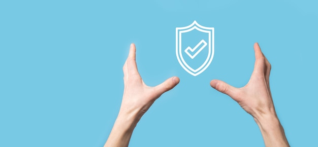 Mano masculina que sostiene el escudo de protección con un icono de marca de verificación en la superficie azul