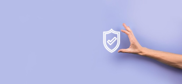 Mano masculina que sostiene el escudo protector con un icono de marca de verificación sobre fondo azul. Equipo de seguridad de red de protección y seguro su concepto de datos.