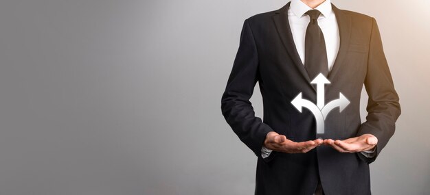 Mano masculina que sostiene el icono con el icono de tres direcciones sobre fondo oscuro. Duda, tener que elegir entre tres opciones diferentes indicadas por flechas que apuntan en dirección opuesta al concepto. Formas.