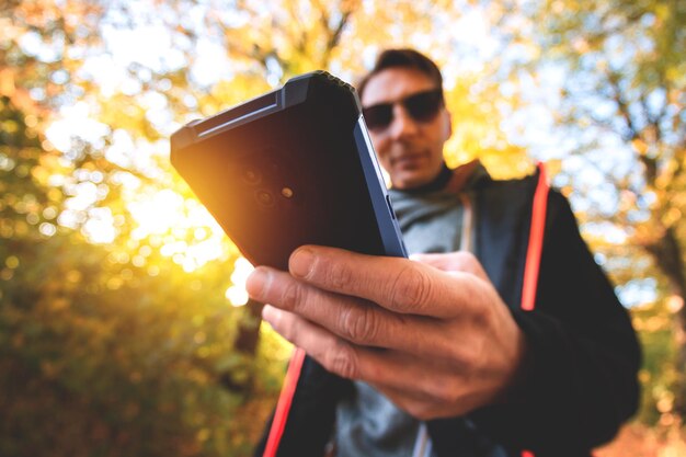 Una mano masculina que sostiene un teléfono móvil que intenta capturar los colores asombrosos del otoño en el bosque