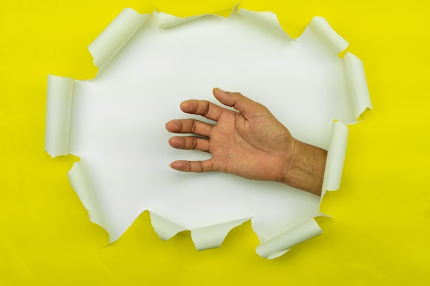 Foto la mano masculina rasgó el papel amarillo en el fondo blanco, espacio para su mensaje en el papel rasgado.