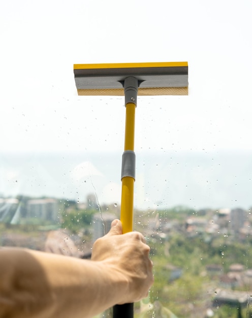 Mano masculina con raspador de cepillo de limpieza de ventanas en el fondo de vidrio húmedo sucio Concepto de servicio de lavado de ventanas