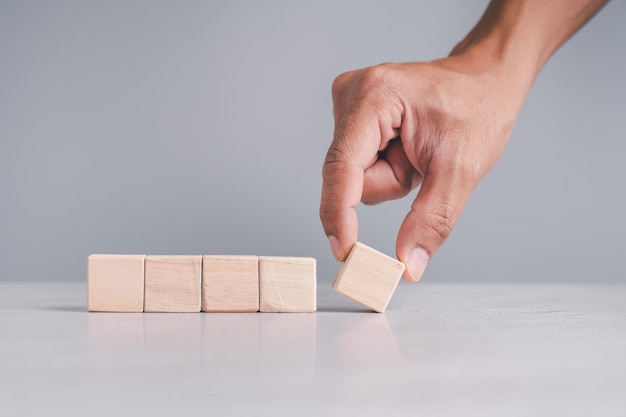 Foto mano masculina recogiendo bloques de madera dispuestos sobre un fondo gris