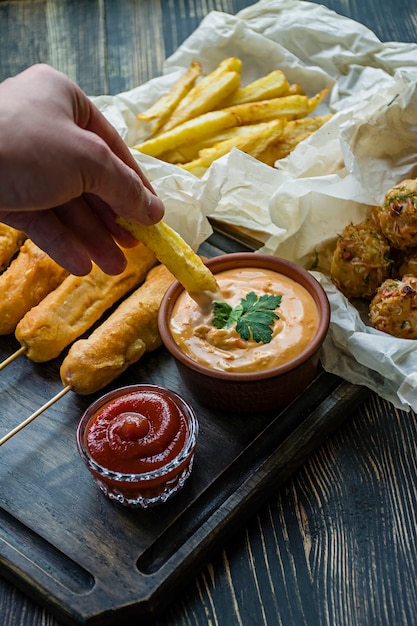 Mano masculina en una salsa de papas fritas. Croquetas de papas fritas, maíz y col.