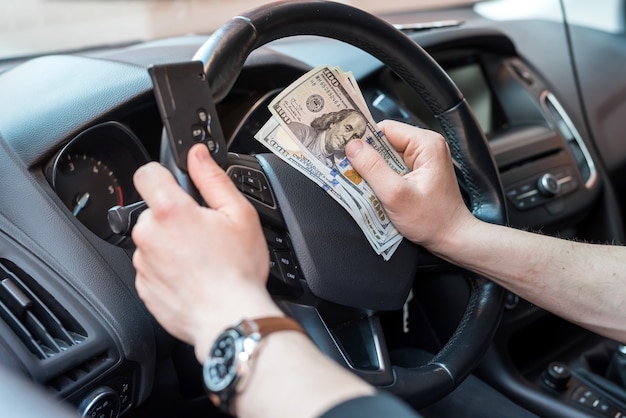 Mano masculina sentada en el coche sosteniendo el dólar y el concepto de finanzas clave del coche