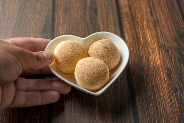 Mano masculina sirviendo pan de queso en un recipiente en forma de corazón sobre una mesa de madera