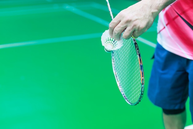 La mano masculina de un solo jugador del bádminton sostiene la polla blanca del transbordador junto con la raqueta