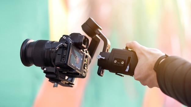 Mano masculina sosteniendo una cámara en Steadycam, fondo de color