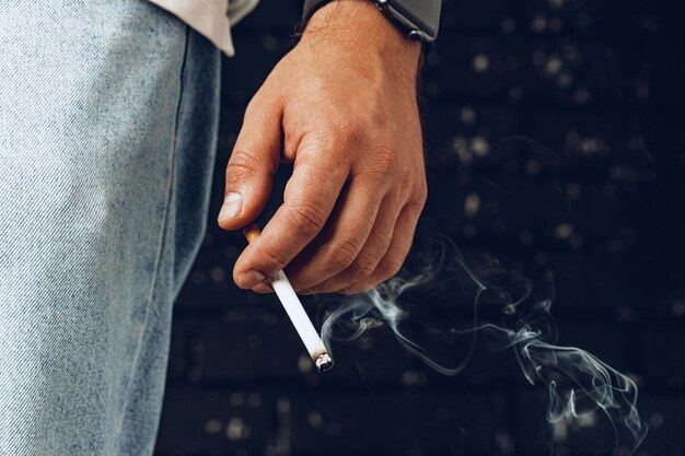 Mano masculina sosteniendo cigarrillo encendido contra fondo negro