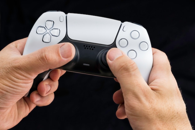 Mano masculina sosteniendo un controlador de juego blanco de próxima generación aislado sobre fondo negro.