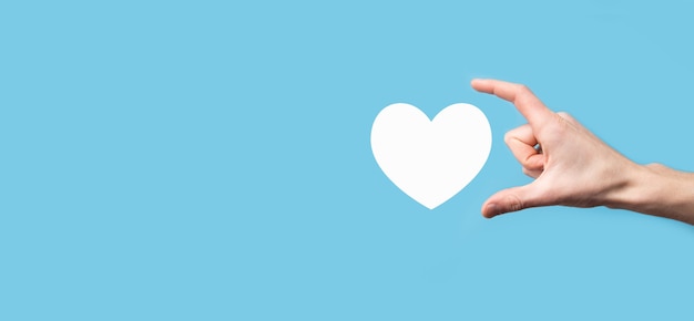 Mano masculina sosteniendo el corazón, como icono sobre fondo azul. Bondad, caridad, amor puro y concepto de compasión.