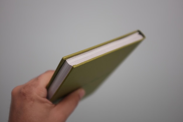 Mano masculina sosteniendo un libro verde contra la pared