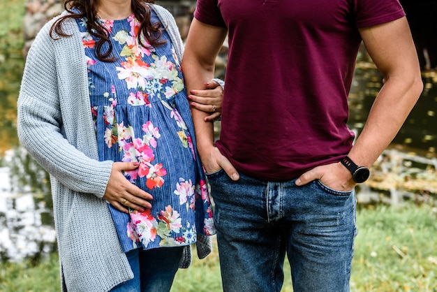 Mano masculina sosteniendo la mano de su esposa embarazada. Mujer embarazada abrazando la barriga.