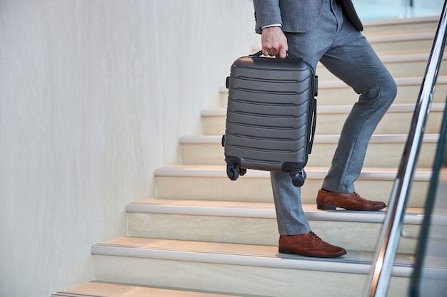 Foto mano masculina sosteniendo un pequeño equipaje de mano en una escalera