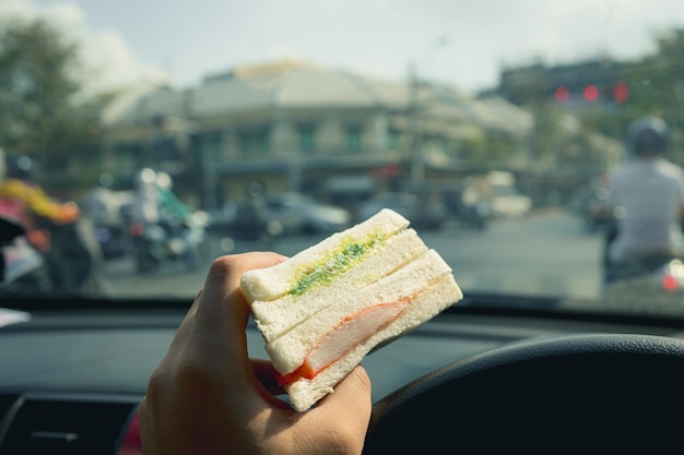 Mano masculina sosteniendo un sándwich en el auto