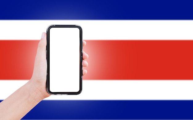 Mano masculina sosteniendo el teléfono inteligente con pantalla en blanco en el fondo de la bandera borrosa de Costa Rica Vista de cierre