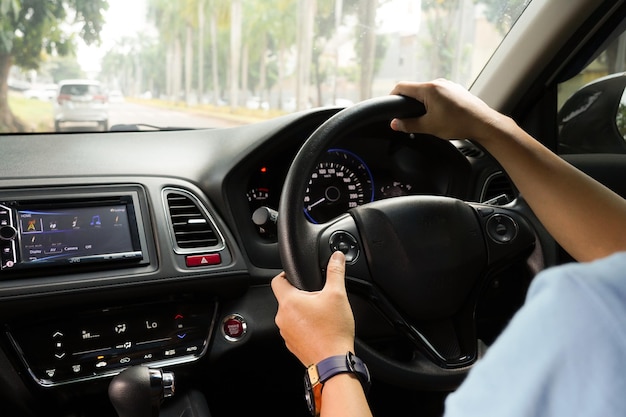 Mano masculina sosteniendo el volante del coche y la vista del salpicadero del coche