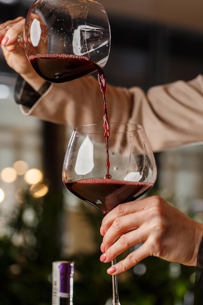 La mano masculina sostiene hermosas copas transparentes para vino de Borgoña en las que se vierte vino tinto de otra copa