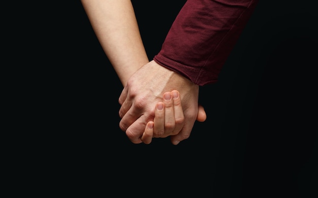 Mano masculina sostiene la mano femenina sobre fondo oscuro