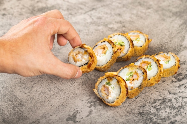 Mano masculina tomando sushi roll colocado sobre una mesa de piedra.