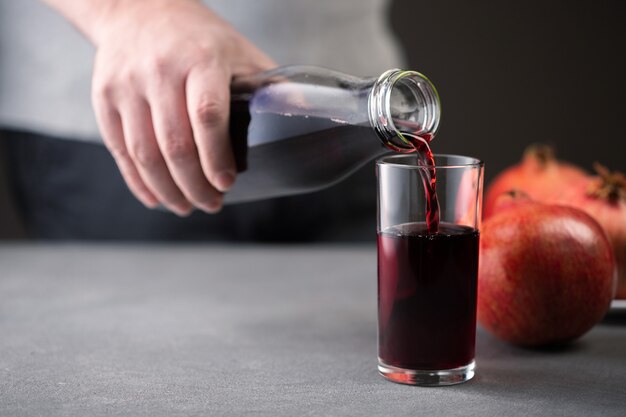 Mano masculina vertiendo jugo de granada de una botella en un vaso