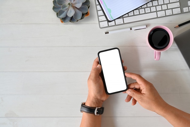 Mano masculina de la vista superior que sostiene los accesorios elegantes móviles del teléfono y de la oficina de la pantalla en blanco