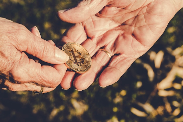 La mano mayor de la mujer está sosteniendo la moneda del bitcoin que da a la mano mayor del hombre en la naturaleza verde