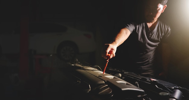 Foto la mano mecánica está tirando de la varilla medidora para verificar el nivel de aceite del motor y la doble exposición del taller de reparación de automóviles