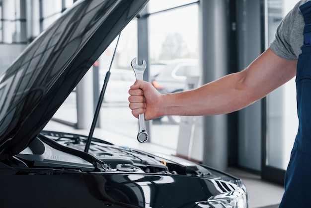 La mano de un mecánico de automóviles con una llave en una zona combinada cerca del automóvil en el taller.