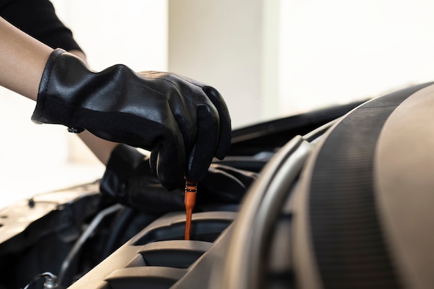 La mano del mecánico de automóviles revisa el aceite del motor para el mantenimiento en el garaje de servicio.