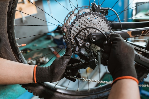 Mano de mecánico de bicicletas masculino en guantes sujeta la cadena sobre la rueda dentada