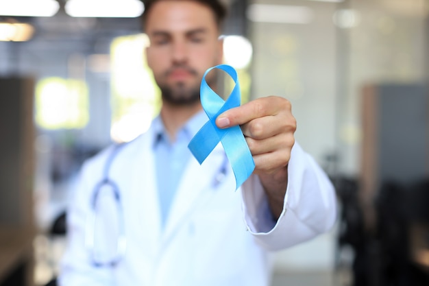 Mano del médico con cinta azul de concienciación sobre el cáncer de próstata. Símbolo del cielo del primer de la oncología de la medicina.