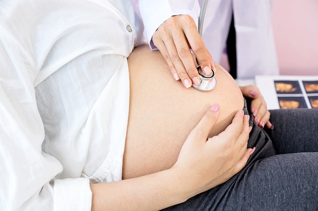 Foto mano de médico con estetoscopio en el estómago de las mujeres embarazadas en el hospital.