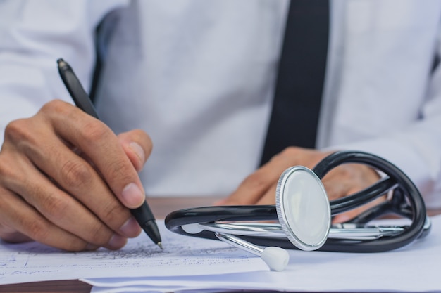 Foto la mano del médico firma la aprobación del paciente, la frecuencia cardíaca de la prueba del estetoscopio del médico