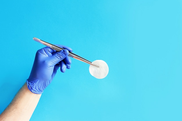 La mano del médico en un guante azul con un par de pinzas