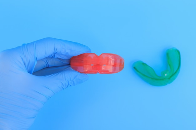 La mano del médico en un guante azul sostiene un entrenador miofuncional para la corrección de los dientes. Enfoque selectivo del espacio azul.