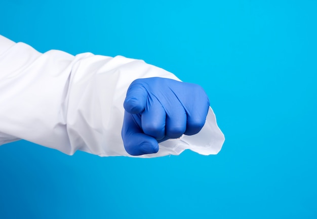 Mano del médico en guante de látex azul y bata blanca, el dedo índice se estira hacia adelante