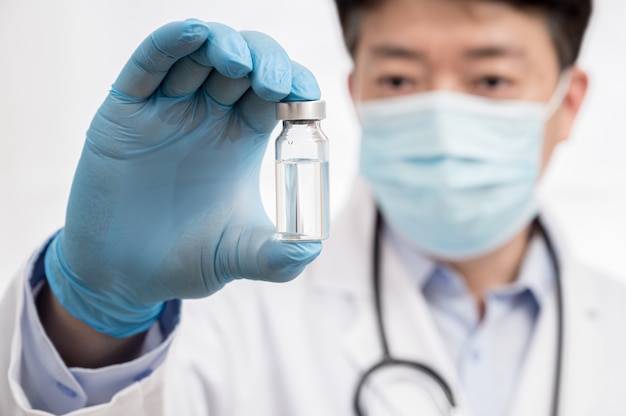 La mano del médico con guantes azules sobre fondo blanco y sosteniendo la vacuna Covid-19.