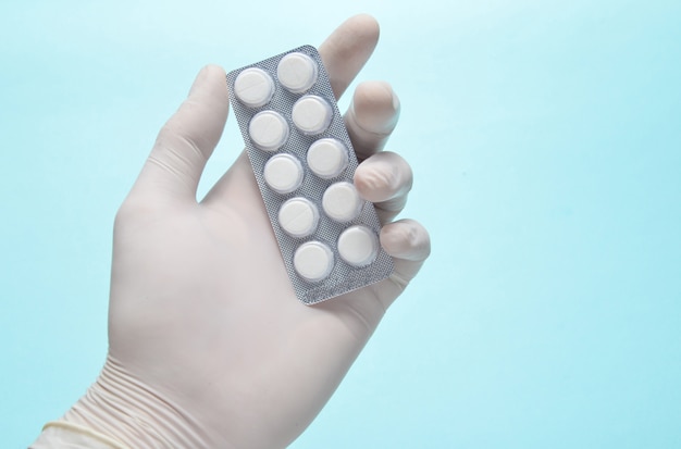 La mano del médico con guantes de látex blancos sostiene una ampolla de pastillas en un azul.
