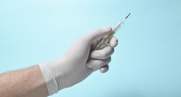 La mano del médico con guantes de látex blancos sostiene el termómetro en un azul.