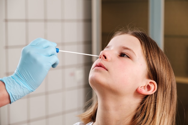 La mano del médico con un hisopo de algodón toma un análisis de la nariz de una niña.