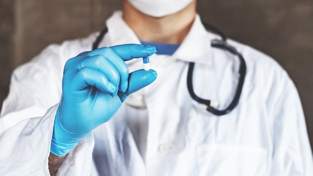 La mano de un médico o farmacéutico en guantes azules sostiene una cápsula con medicamento