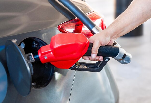 La mano mexicana de un hombre bombeando gasolina manguera roja y primer plano de coche gris