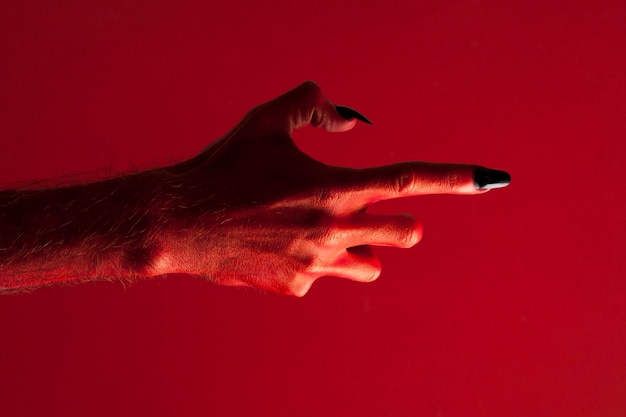 Foto mano de monstruo del diablo rojo de halloween con uñas negras contra un fondo rojo