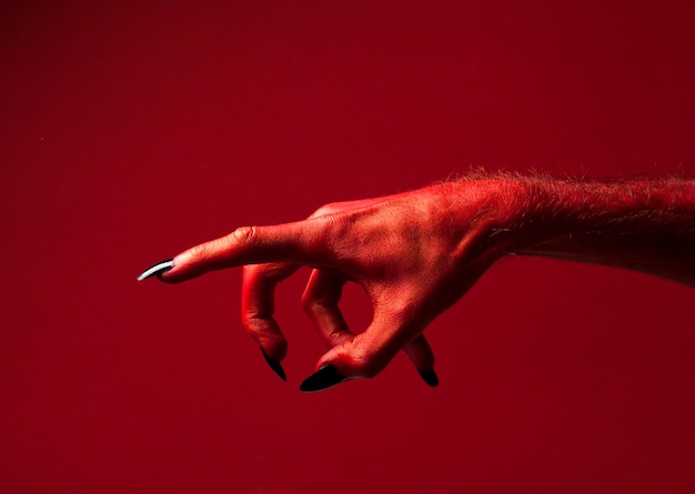 Mano de monstruo del diablo rojo de Halloween con uñas negras contra un fondo rojo