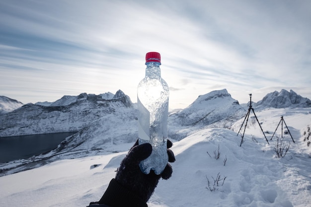 Mano de montañero sosteniendo una botella de agua en una montaña cubierta de nieve por la mañana